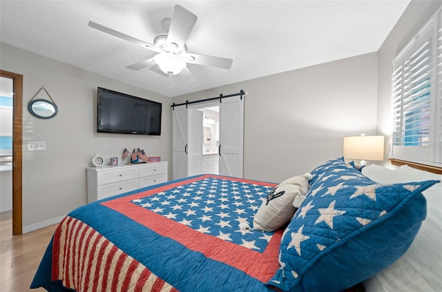 bedroom featuring a barn door, ceiling fan, light hardwood / wood-style floors, and a textured ceiling