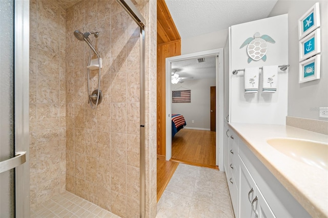 bathroom with vanity, a textured ceiling, ceiling fan, tiled shower, and wood-type flooring