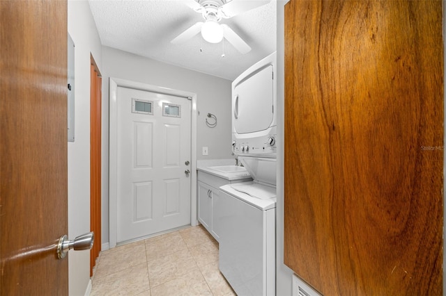 laundry room featuring cabinets, a textured ceiling, ceiling fan, light tile patterned floors, and stacked washer / dryer