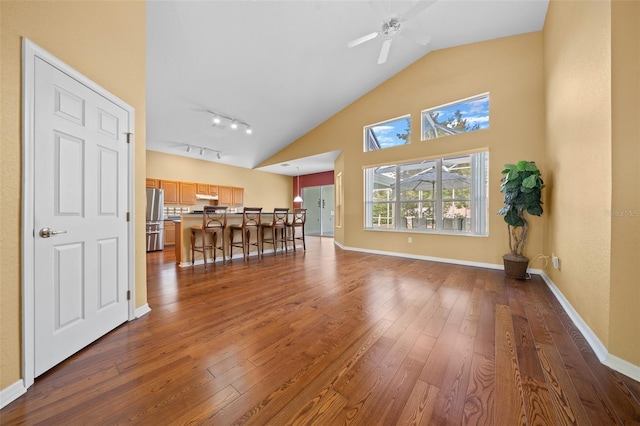 living room with dark wood-type flooring, a ceiling fan, track lighting, high vaulted ceiling, and baseboards