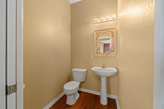 bathroom featuring baseboards, a textured wall, toilet, wood finished floors, and a sink