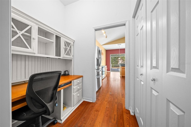 home office with dark wood-type flooring, lofted ceiling, built in desk, and baseboards