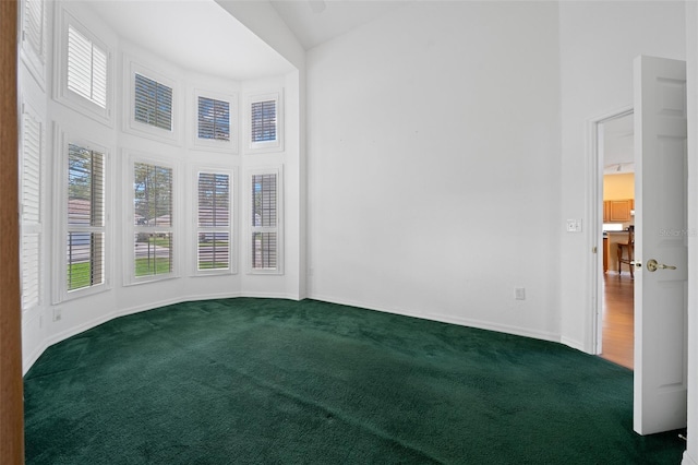 unfurnished room with high vaulted ceiling, baseboards, dark carpet, and a wealth of natural light