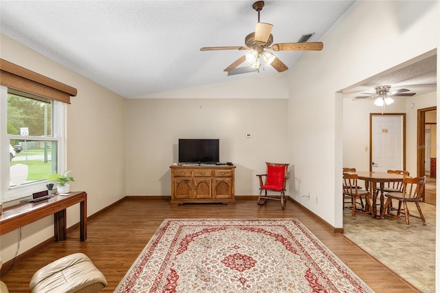 living room featuring a textured ceiling, vaulted ceiling, ceiling fan, and light hardwood / wood-style flooring