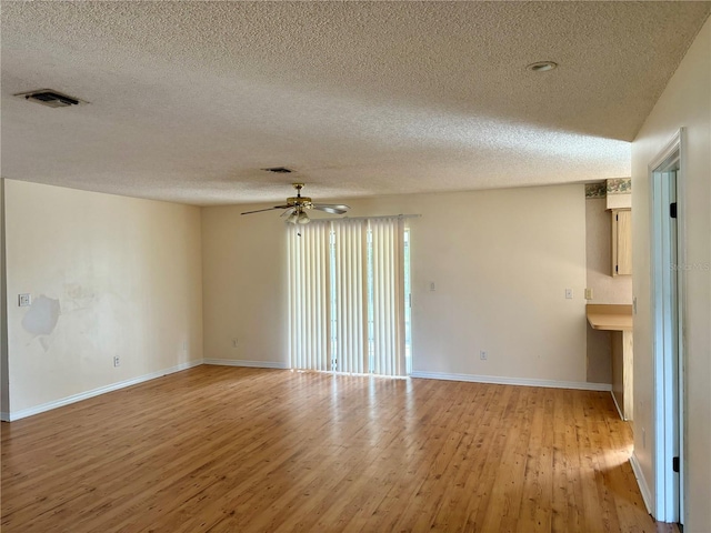 empty room with ceiling fan, light wood-type flooring, and a textured ceiling