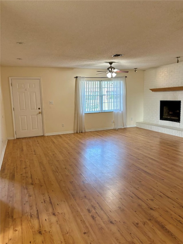 unfurnished living room featuring a textured ceiling, hardwood / wood-style flooring, a brick fireplace, and ceiling fan