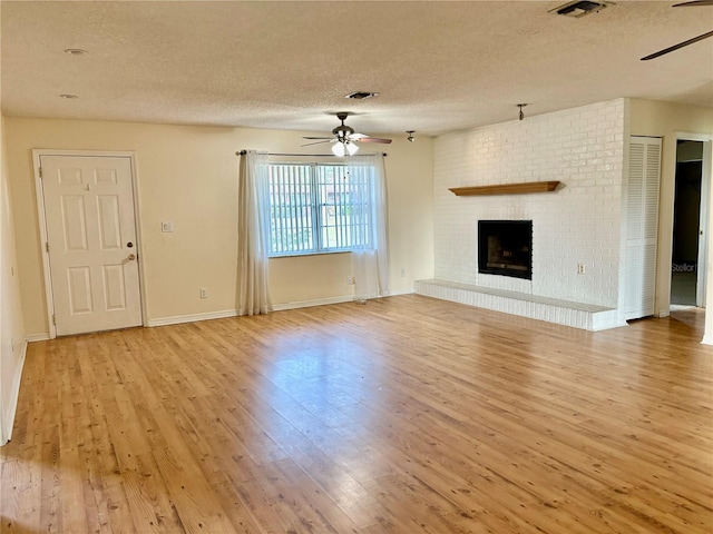 unfurnished living room with ceiling fan, light hardwood / wood-style floors, a textured ceiling, and a brick fireplace