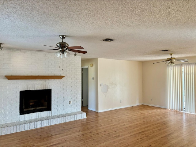 unfurnished living room with hardwood / wood-style floors, a textured ceiling, and a brick fireplace