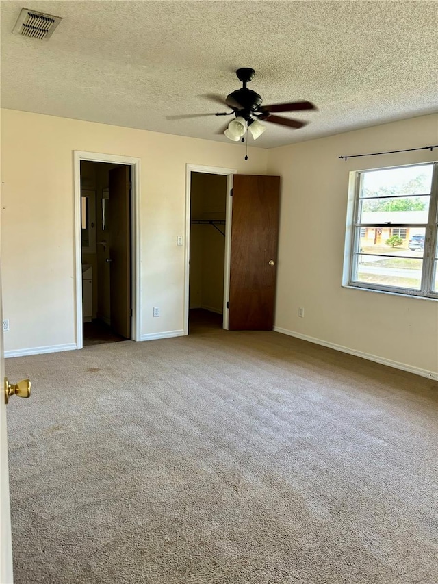 unfurnished bedroom featuring a walk in closet, light colored carpet, and ceiling fan