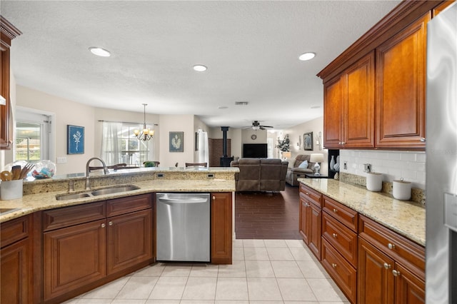 kitchen featuring sink, light stone counters, appliances with stainless steel finishes, hanging light fixtures, and a wood stove