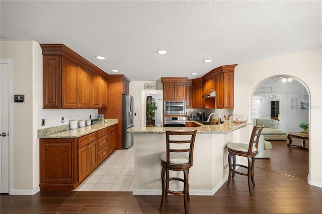 kitchen with stainless steel appliances, light hardwood / wood-style floors, light stone counters, kitchen peninsula, and a textured ceiling