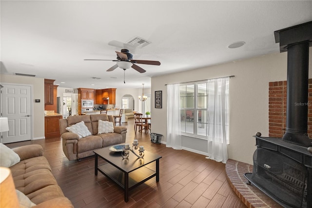 living room with a wood stove, ceiling fan with notable chandelier, and dark wood-type flooring