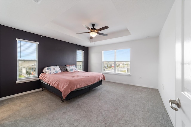 carpeted bedroom with ceiling fan and a tray ceiling