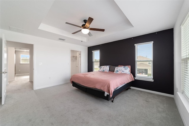 bedroom featuring ceiling fan, multiple windows, light carpet, and a walk in closet