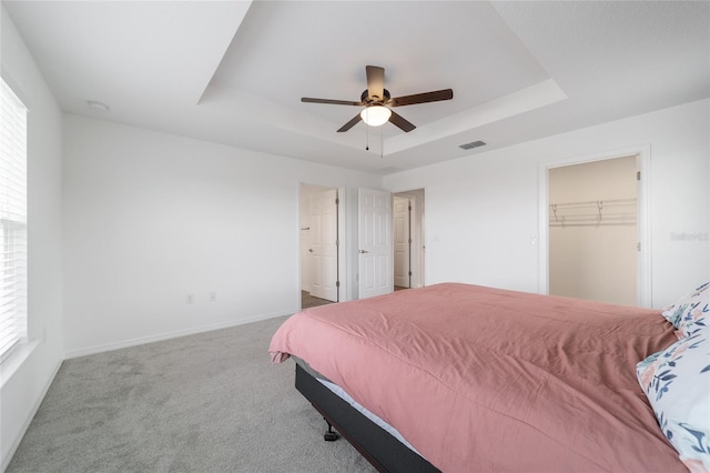 bedroom with ceiling fan, light carpet, a closet, and a tray ceiling