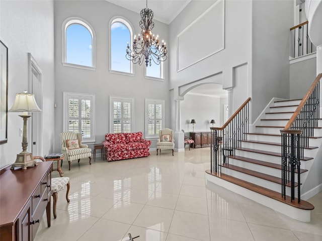 tiled entrance foyer featuring decorative columns, a chandelier, and a towering ceiling