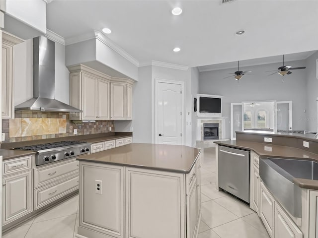 kitchen with appliances with stainless steel finishes, wall chimney exhaust hood, a kitchen island, decorative backsplash, and cream cabinetry