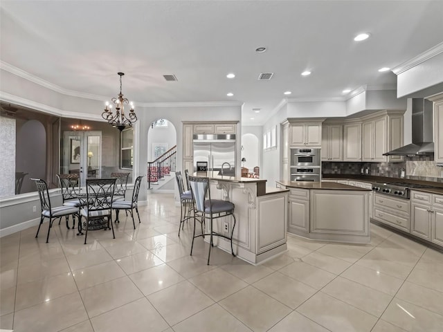 kitchen featuring wall chimney exhaust hood, decorative light fixtures, stainless steel appliances, decorative backsplash, and a center island with sink