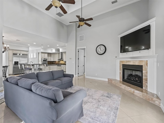 tiled living room with ornamental molding, ceiling fan with notable chandelier, and a tile fireplace