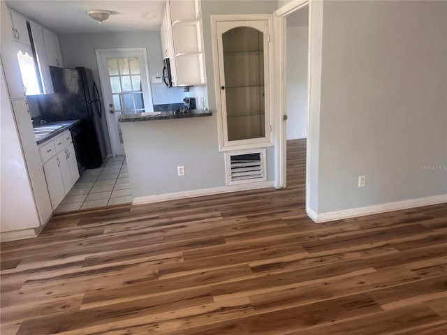 kitchen with kitchen peninsula, white cabinetry, black refrigerator, and dark wood-type flooring