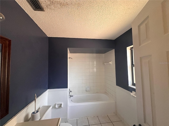 bathroom featuring tile patterned flooring, tiled shower / bath combo, toilet, and a textured ceiling