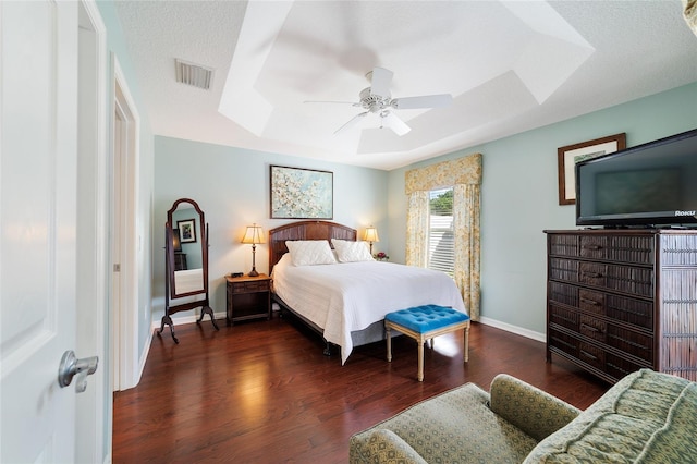 bedroom with a textured ceiling, a raised ceiling, ceiling fan, and dark wood-type flooring