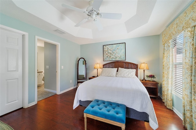 bedroom with a tray ceiling, ensuite bath, ceiling fan, and dark wood-type flooring