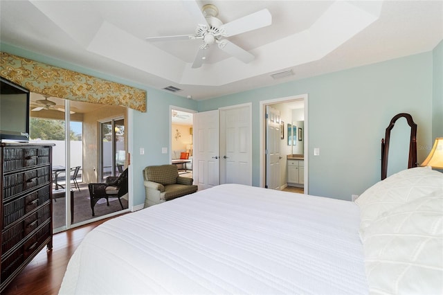 bedroom featuring ensuite bath, ceiling fan, access to exterior, hardwood / wood-style floors, and a tray ceiling