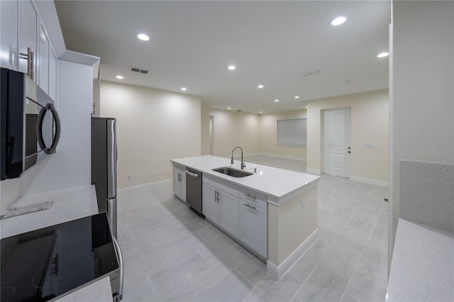 kitchen featuring light stone countertops, white cabinetry, stainless steel appliances, an island with sink, and sink