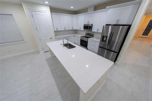 kitchen featuring sink, appliances with stainless steel finishes, an island with sink, white cabinets, and light stone counters