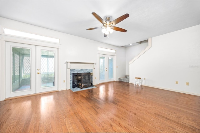 unfurnished living room with french doors, light wood-type flooring, a stone fireplace, and ceiling fan