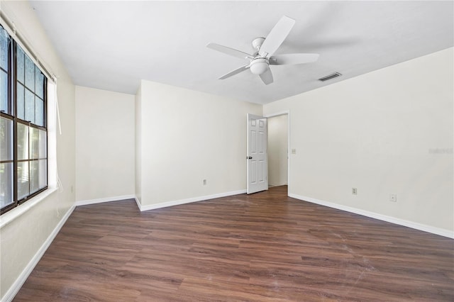 empty room featuring ceiling fan, a healthy amount of sunlight, and dark wood-type flooring