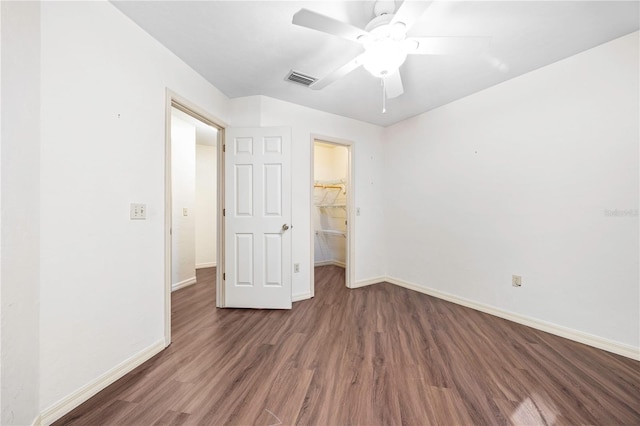 unfurnished bedroom with a walk in closet, ceiling fan, a closet, and dark wood-type flooring