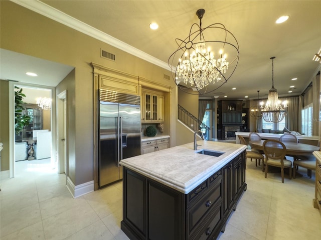 kitchen featuring crown molding, sink, light tile patterned floors, a center island with sink, and built in fridge