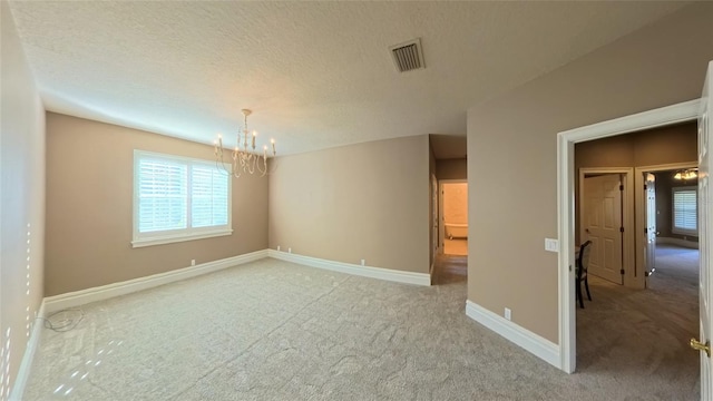 carpeted empty room with a textured ceiling and a notable chandelier