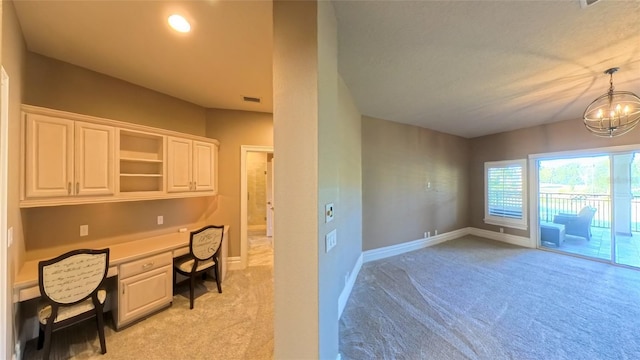 carpeted home office featuring a notable chandelier and built in desk