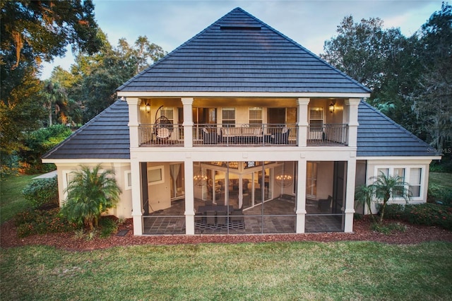 rear view of property featuring a sunroom, a balcony, and a lawn