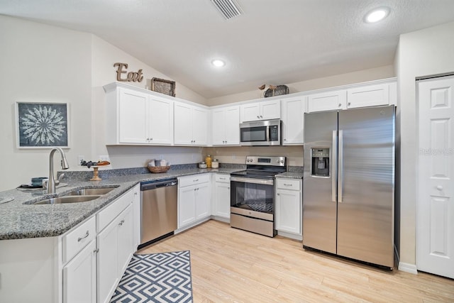 kitchen with light hardwood / wood-style floors, sink, appliances with stainless steel finishes, white cabinets, and vaulted ceiling