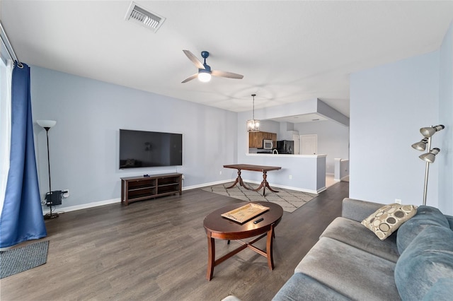 living room featuring ceiling fan with notable chandelier and dark wood-type flooring