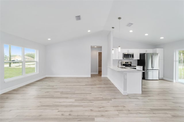 kitchen featuring kitchen peninsula, pendant lighting, vaulted ceiling, white cabinets, and appliances with stainless steel finishes