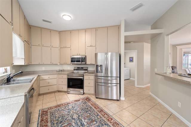 kitchen with washer / dryer, appliances with stainless steel finishes, light tile patterned flooring, cream cabinets, and sink