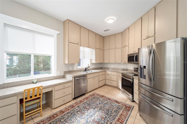 kitchen with light tile patterned floors, appliances with stainless steel finishes, cream cabinetry, and sink