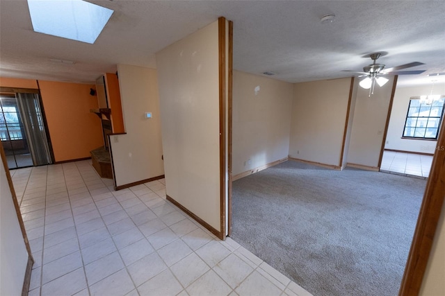 unfurnished room featuring light carpet, a textured ceiling, a skylight, and ceiling fan