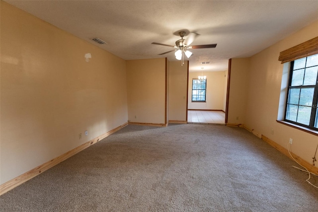 spare room with a textured ceiling, light colored carpet, and ceiling fan with notable chandelier