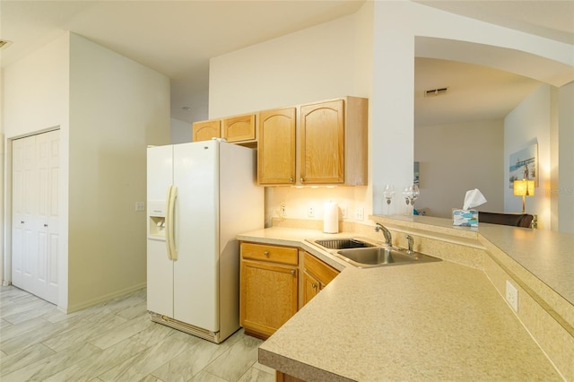 kitchen with kitchen peninsula, white fridge with ice dispenser, light brown cabinets, and sink