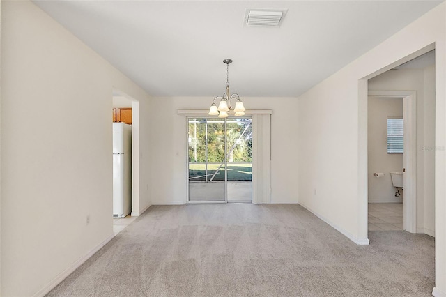 spare room featuring light carpet and an inviting chandelier