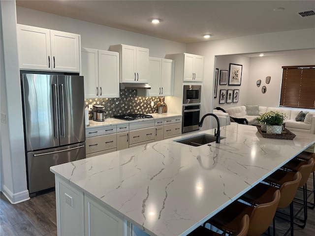 kitchen with stainless steel appliances, dark hardwood / wood-style flooring, a center island with sink, light stone counters, and white cabinets