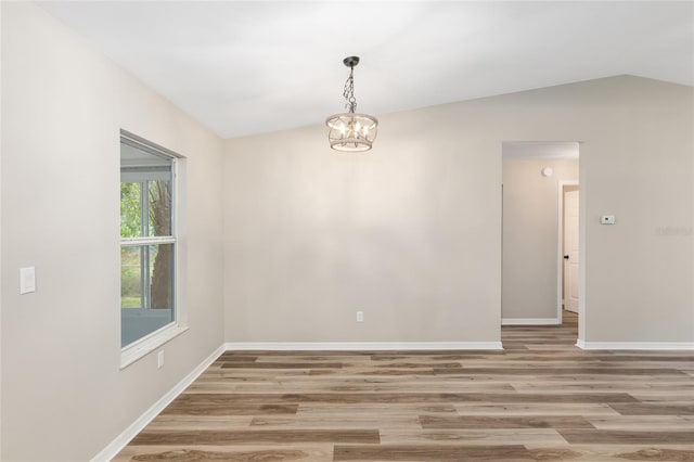 empty room with vaulted ceiling, hardwood / wood-style flooring, and an inviting chandelier