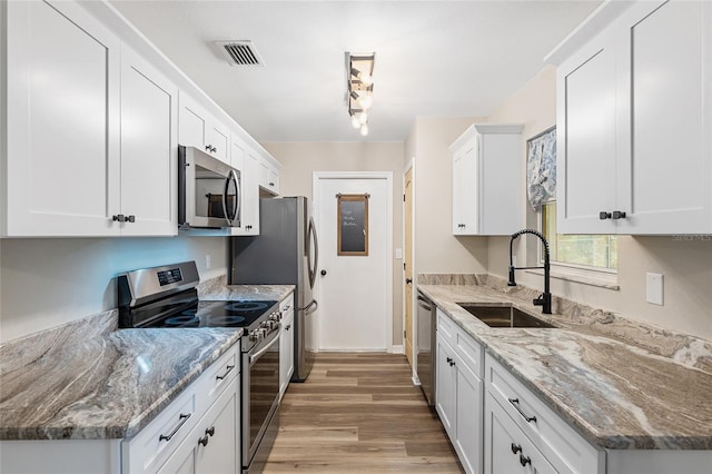 kitchen featuring light stone countertops, appliances with stainless steel finishes, sink, light hardwood / wood-style flooring, and white cabinetry