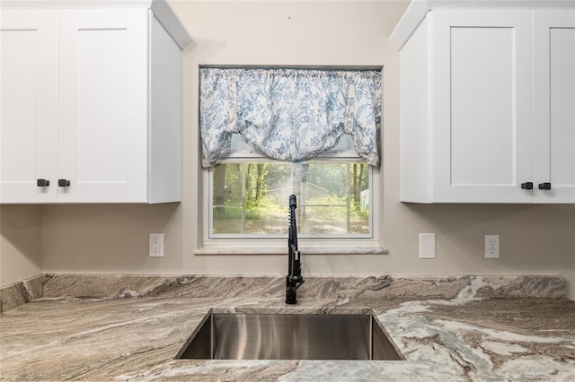 kitchen featuring light stone counters, sink, and white cabinets